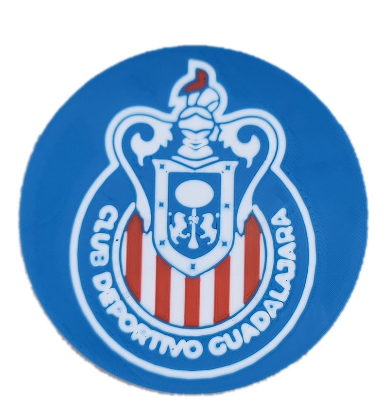 Puede incluir: Un emblema circular azul y blanco con un escudo a rayas rojas y blancas y el texto "Club Deportivo Guadalajara" en un c&iacute;rculo blanco.
