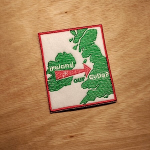 Può includere: Una toppa ricamata bianca con una mappa verde delle isole britanniche. Una freccia punta dall'Irlanda al Regno Unito con il testo "La nostra Cuba?"