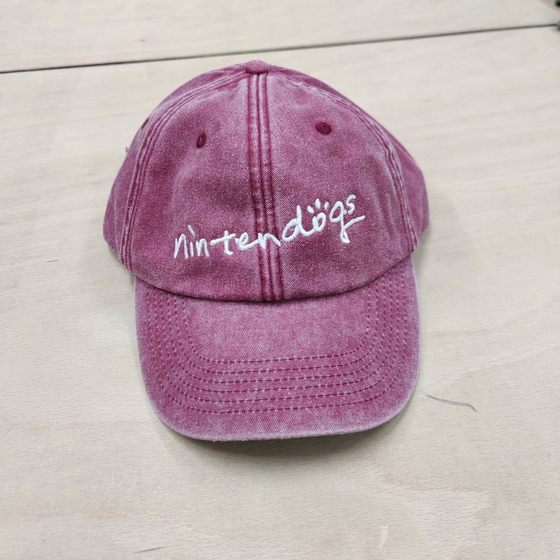 K&ouml;nnte beinhalten: Eine burgunderfarbene Baseballkappe mit dem Schriftzug "nintendogs" in wei&szlig; auf der Vorderseite.
