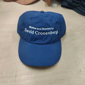 以下が含まれることがあります： 「Written and Directed by David Cronenberg」と白く刺繍された青い野球帽。