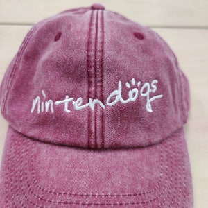 K&ouml;nnte beinhalten: Eine rote Baseballkappe mit einem wei&szlig;en gestickten Logo, auf dem "nintendogs" steht.