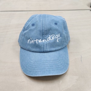 K&ouml;nnte beinhalten: Eine hellblaue Baseballkappe aus Denim mit wei&szlig; gesticktem Text, der "nintendogs" lautet