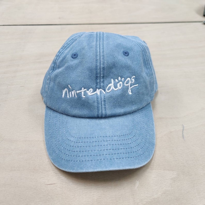 K&ouml;nnte beinhalten: Eine hellblaue Baseballkappe aus Denim mit wei&szlig; gesticktem Text, der "nintendogs" lautet