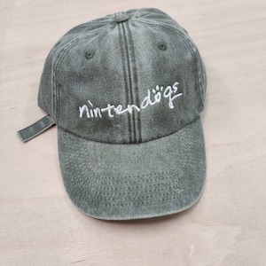 K&ouml;nnte beinhalten: Eine gr&uuml;ne, abgenutzte Baseballkappe aus Baumwolle mit einem wei&szlig;en gestickten Logo, auf dem "nintendogs" steht.