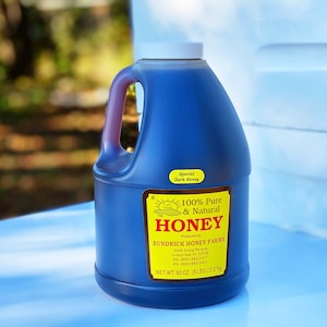 May include: A blue plastic jug of 100% pure and natural honey, labeled "Special Dark Honey", produced by Bundrick Honey Farms. The jug contains 80 ounces (5 lbs) of honey.