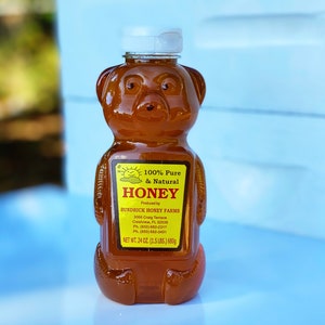May include: A bear-shaped honey bottle filled with amber-colored honey. The label reads "100% Pure & Natural Honey" and lists the producer, Bundrick Honey Farms. The bottle contains 24 oz (1.5 lbs) or 680g of honey.