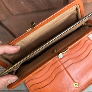May include: A vintage orange leather wallet with a snap closure and multiple card slots. The wallet is open to reveal the interior lining.
