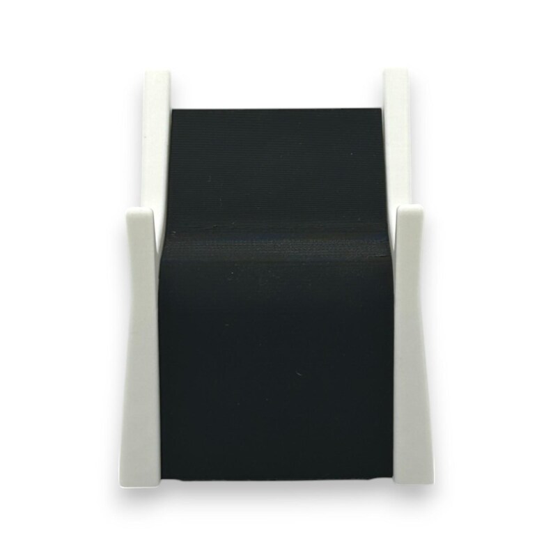 以下が含まれることがあります： 白と黒のミニマリストなデスクオーガナイザー。オーガナイザーは、2つの白い垂直サポートで支えられた黒い長方形のベースを備えています。サポートは曲線的なデザインで、シンプルな構造にエレガンスを加えています。