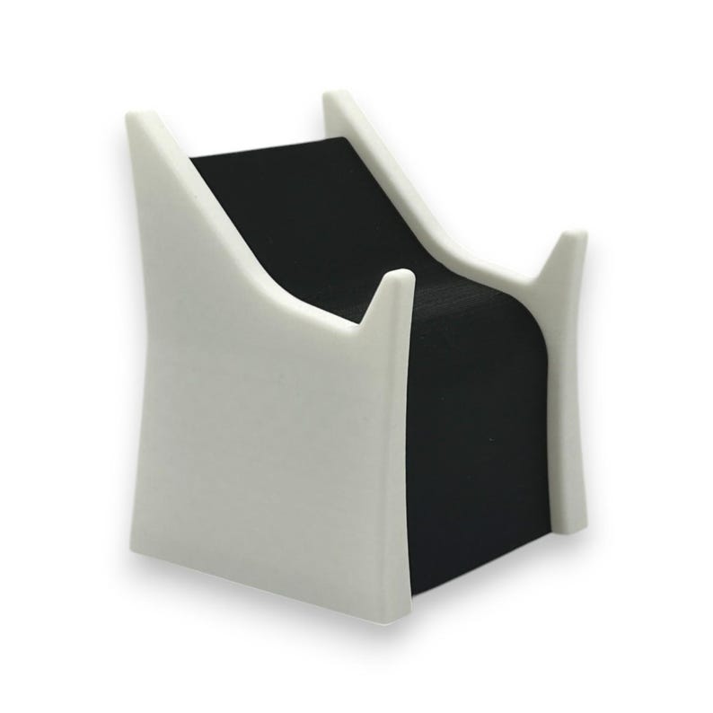 以下が含まれることがあります： 黒いベルベットのインサートが付いた、白くモダンなジュエリーディスプレイスタンド。スタンドは、2つの直立したサポートを備えた湾曲したデザインです。スタンドはネックレスやブレスレットを保持するように設計されています。