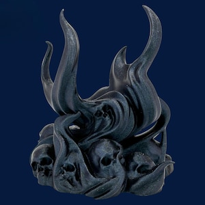 May include: A dark sculpture depicting skulls and flame-like forms. The piece is a dark colour, possibly metallic, with a textured surface. The design evokes a gothic or fantasy aesthetic. The sculpture's details are intricate.