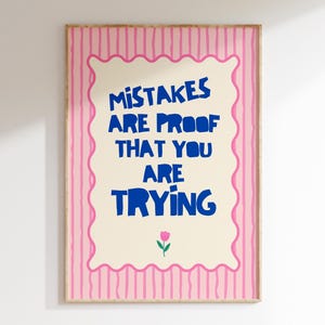 Könnte beinhalten: Ein rechteckiger Wandkunstdruck mit hellrosa Hintergrund und vertikalen dunkelrosa Streifen. Ein cremefarbenes Mittelfeld mit gewelltem rosa Rand enthält den blauen Text: MISTAKES ARE PROOF THAT YOU ARE TRYING, sowie eine kleine rosa Tulpe.