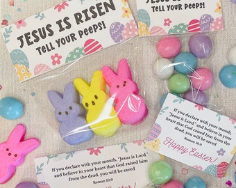 May include: A clear plastic bag filled with pastel-colored candy eggs and marshmallow chicks. The bag includes two cards with the text "Jesus is Risen, Tell Your Peeps!" and a Bible verse about salvation. The cards are decorated with floral patterns and Easter eggs.