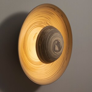May include: A circular wall sconce with a layered, wood-like design. The light fixture has a warm, yellow glow emanating from the center.