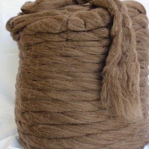 May include: A large roll of brown wool roving. The roving is tightly wound and has a soft, fluffy texture.