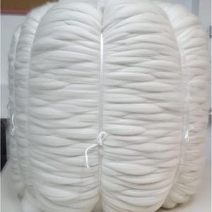 Puede incluir: Un gran paquete de fibra de lana blanca, atado con una cuerda. La lana está bien compacta y tiene una textura suave y esponjosa.
