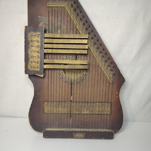 May include: Vintage wooden zither with strings, brass frets, and a decorative sound hole. The instrument has a dark brown finish with visible wear and tear, and a small label that reads "Conservatory".