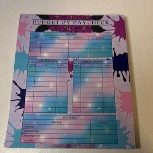 May include: A pink and blue budget tracker with a galaxy design. The tracker has sections for income, bills and debt, sinking funds, and a summary. The text "BUDGET BY PAYCHECK" is at the top of the page.