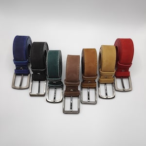 Pode incluir: Sete cintos de couro em diferentes cores, incluindo azul, preto, verde, marrom e bege. Cada cinto tem uma fivela prateada e é forrado com costuras brancas.