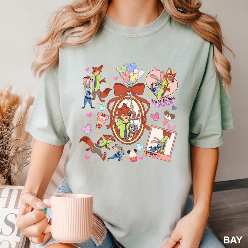 Op de afbeelding: Lichtgroen T-shirt met cartoonfiguren uit Zootopia. Het ontwerp bevat afbeeldingen van Nick Wilde en Judy Hopps, samen met de woorden "Best Friends Forever" en "Bestie". Het shirt heeft een ronde hals en korte mouwen.