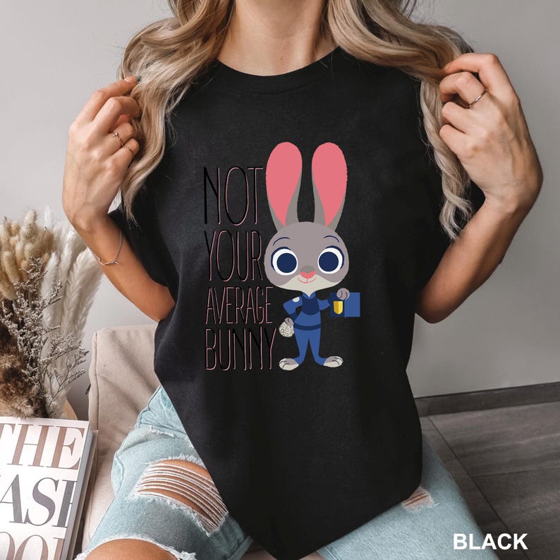May include: Black t-shirt with a cartoon illustration of a bunny in a police uniform. The text reads "NOT YOUR AVERAGE BUNNY". The bunny has pink ears and is holding a badge and a blue briefcase. The shirt is black.