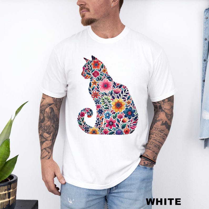 May include: White t-shirt featuring a colorful floral cat design. The cat silhouette is filled with various flowers in shades of pink, orange, blue, and yellow. The word "WHITE" is printed in bold, black letters at the bottom of the image.