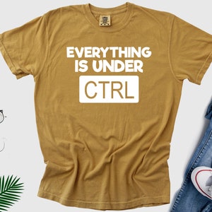 May include: A mustard yellow t-shirt with the text "EVERYTHING IS UNDER CTRL" in white.