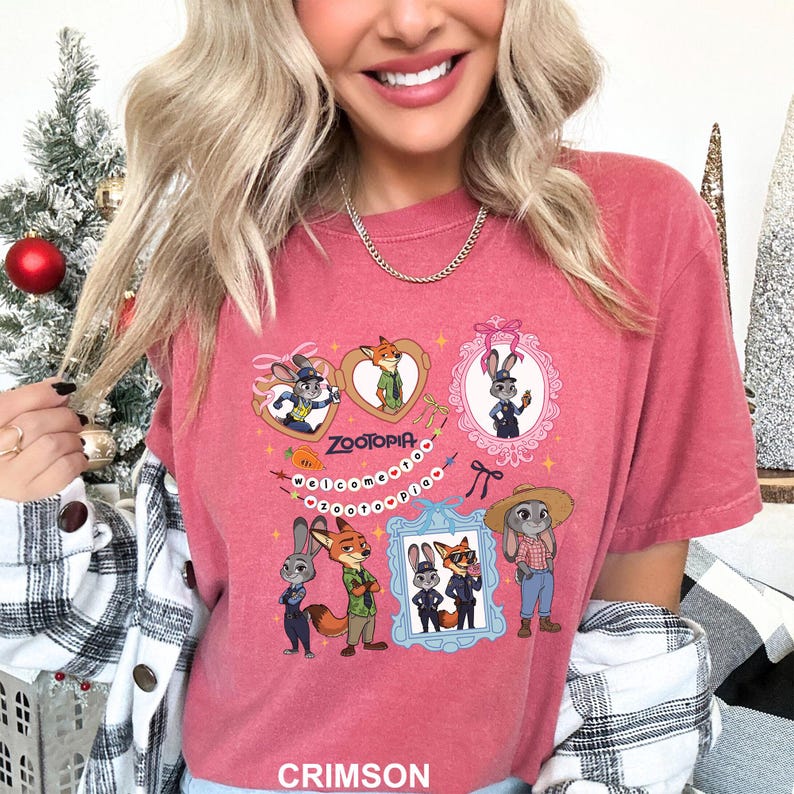 Op de afbeelding: Karmizijnrood T-shirt met cartoonfiguren uit Zootopia. Het ontwerp bevat ingelijste afbeeldingen van de personages, het woord "Zootopia" en de zin "Welcome to Zootopia". Het shirt heeft een ronde hals en korte mouwen.