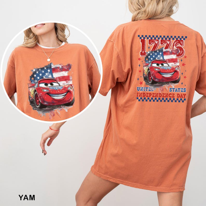 May include: An orange short-sleeve t-shirt featuring a graphic of a red race car with a United States flag background. The back design includes the text 1776 and UNITED STATES INDEPENDENCE DAY with a checkered border and red star accents.