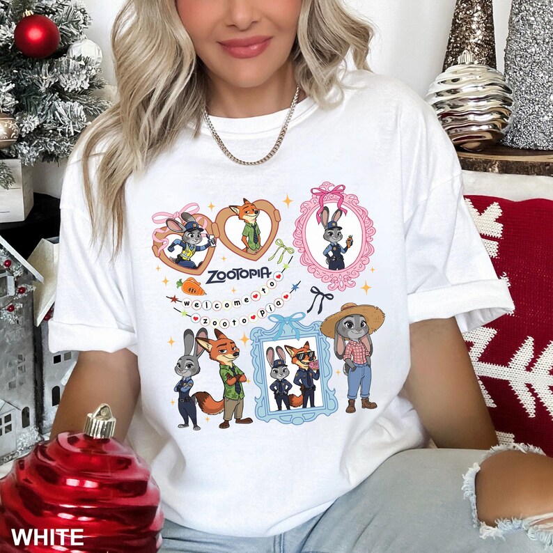 Op de afbeelding: Wit T-shirt met een kleurrijk cartoonontwerp met personages uit de film Zootopia. Het ontwerp bevat ingelijste afbeeldingen van de personages, het woord "Zootopia" en de zin "welcome to zootopia".