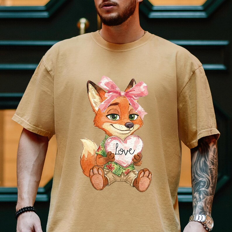 May include: A tan t-shirt featuring a cartoon fox with a pink bow, holding a heart-shaped sign that says "Love". The fox is wearing a Hawaiian shirt and khaki shorts. The shirt has short sleeves.