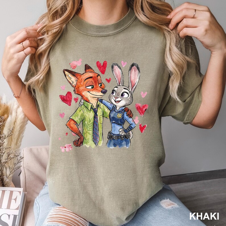 Może przedstawiać: Khaki koszulka z akwarelową ilustracją Nicka Wilde'a i Judy Hopps z Zootopii, otoczonych czerwonymi i r&oacute;żowymi sercami. Nick ma na sobie zieloną koszulę i krawat, a Judy mundur policjantki.