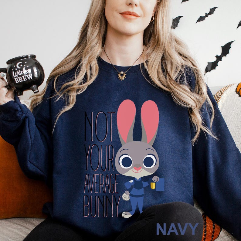 Op de afbeelding: Marineblauw sweatshirt met een cartoon konijn ontwerp en de tekst "NOT YOUR AVERAGE BUNNY". Het konijn heeft roze oren en houdt een blauwe tas vast. Het woord "NAVY" staat onderaan het sweatshirt.
