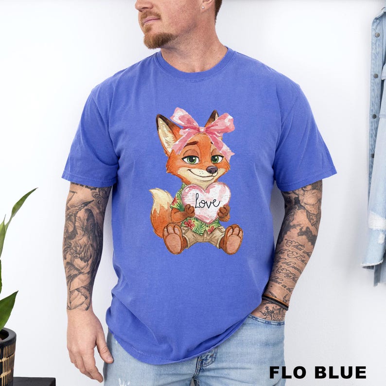 May include: Flo blue t-shirt featuring a cartoon fox holding a heart with the word "love" on it. The fox has a pink bow and is wearing a Hawaiian shirt. The text "FLO BLUE" is at the bottom of the image.