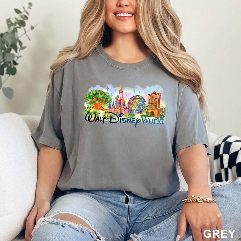 May include: A grey short-sleeve t-shirt featuring a colorful graphic print of the Walt Disney World theme park landmarks, including a tree, a castle, a geodesic sphere, and a tower, with the text Walt Disney World printed in blue script.