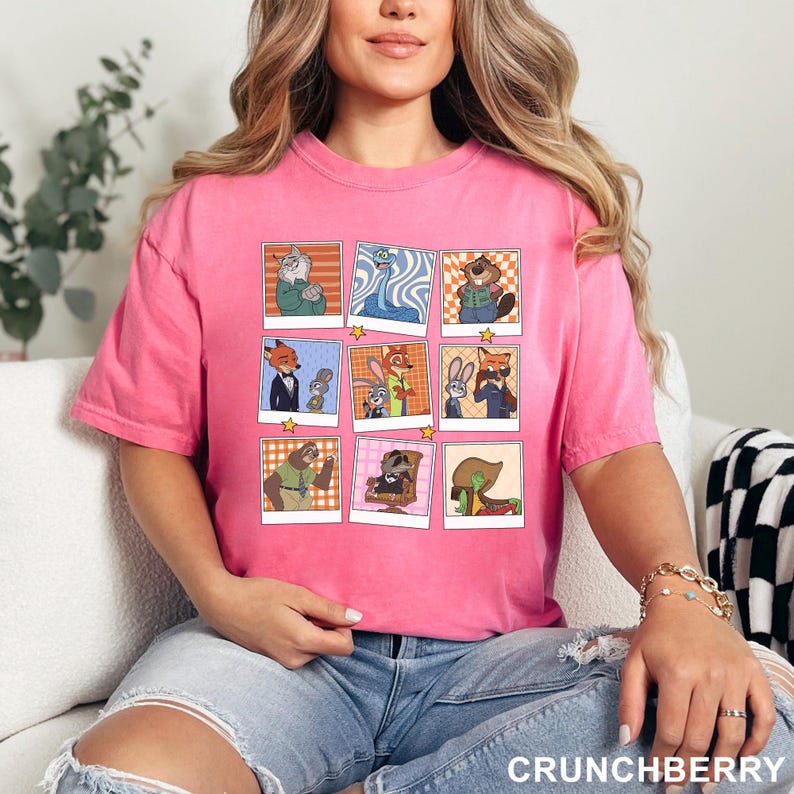 May include: A pink t-shirt featuring a grid of cartoon character images. The images are in a polaroid style with a star in each corner. The text "CRUNCHBERRY" is printed in white at the bottom right.