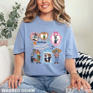 Op de afbeelding: Lichtblauw T-shirt met stripfiguren uit de film Zootopia. Het ontwerp bevat ingelijste afbeeldingen van de personages, het woord "Zootopia" en decoratieve elementen. Het T-shirt is gemaakt van een zacht materiaal.