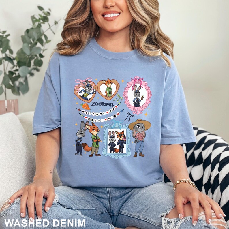 Op de afbeelding: Lichtblauw T-shirt met stripfiguren uit de film Zootopia. Het ontwerp bevat ingelijste afbeeldingen van de personages, het woord "Zootopia" en decoratieve elementen. Het T-shirt is gemaakt van een zacht materiaal.