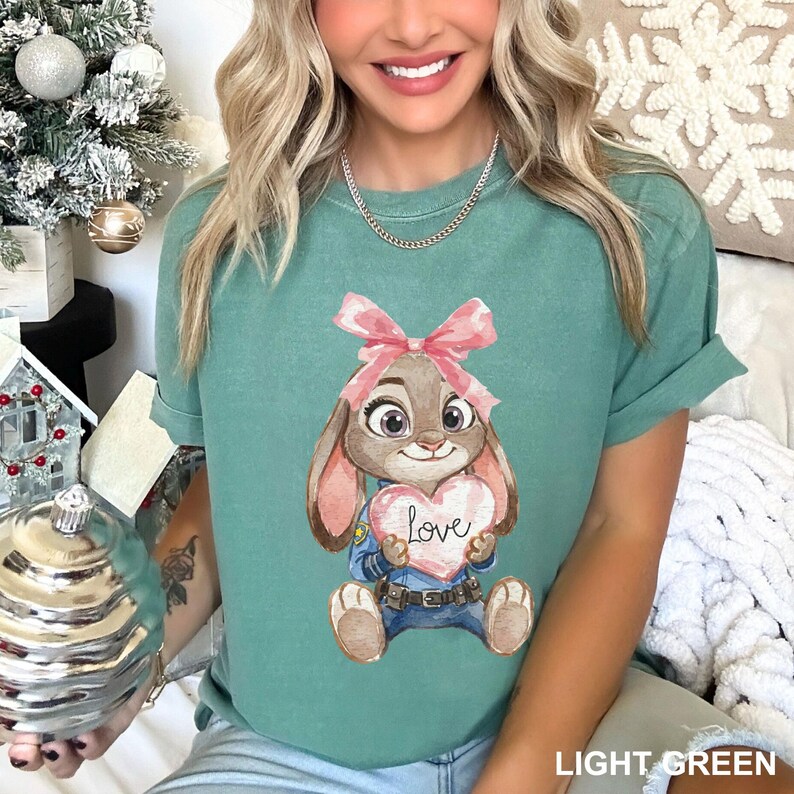 May include: Light green t-shirt featuring a cartoon bunny holding a heart with the word "Love". The bunny wears a pink bow and a police uniform. The text "LIGHT GREEN" is at the bottom right of the shirt.