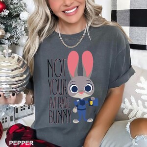 May include: Dark grey t-shirt with a cartoon bunny character in a blue uniform, holding a blue briefcase. The text "NOT YOUR AVERAGE BUNNY" is printed on the shirt in black and pink.