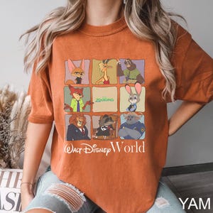 May include: Burnt orange t-shirt featuring a grid of Zootopia characters. The shirt includes images of Nick Wilde, Judy Hopps, and other characters from the Disney movie. The text "Walt Disney World" is printed below the grid.