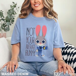 May include: A pale blue t-shirt featuring the phrase "NOT YOUR AVERAGE BUNNY" and a cartoon bunny character. The bunny has pink ears and a police uniform. The words "WASHED DENIM" are at the bottom of the image.