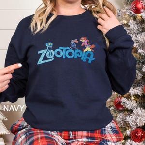 May include: Navy blue crew neck sweatshirt with the word "Zootopia" in light blue, and cartoon characters. The word "NAVY" is printed in white on the bottom left. The sweatshirt is a dark blue colour.