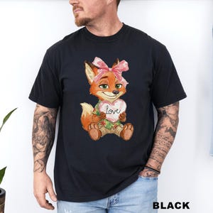 May include: Black t-shirt featuring a cartoon fox with a pink bow, holding a heart-shaped sign that says "Love." The fox is wearing a Hawaiian shirt and khaki shorts. The word "BLACK" is printed at the bottom.