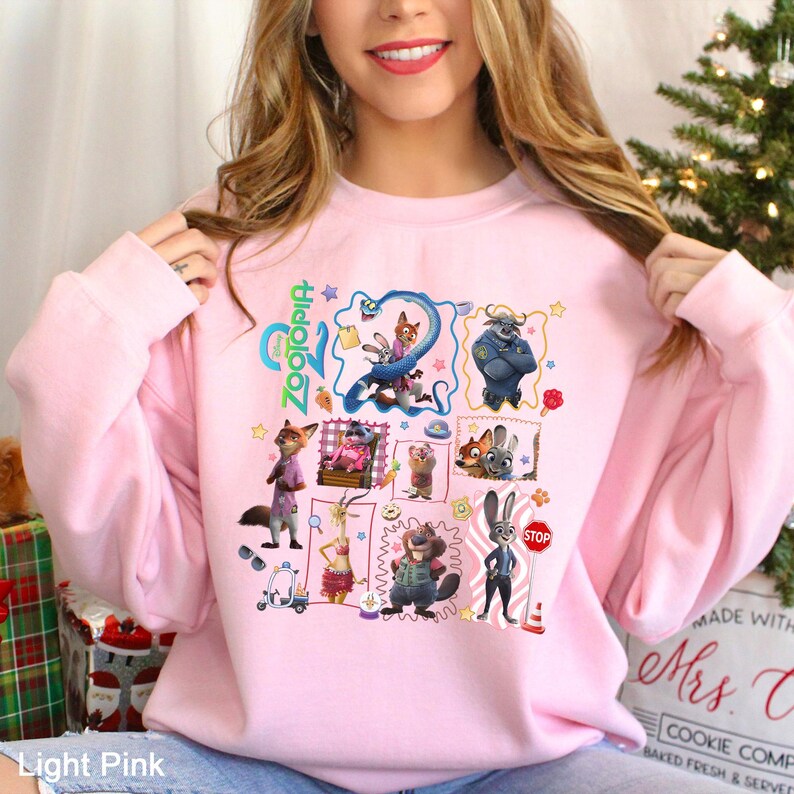 May include: Pale pink sweatshirt with a colourful graphic of Zootopia characters. The design features various animal characters in a grid, with the film's title in green and blue. The sweatshirt is a crew neck style, perfect for casual wear.