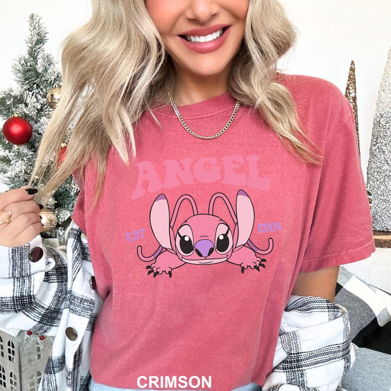 K&ouml;nnte beinhalten: Karmesinrotes T-Shirt mit einem rosa Cartoon-Charakter und dem Wort "ANGEL". Der Charakter hat gro&szlig;e Ohren und liegt. Der Text "EST 2004" befindet sich ebenfalls auf dem T-Shirt.