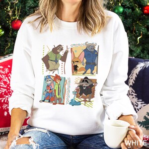 May include: White sweatshirt with cartoon characters from Zootopia. The design includes a sloth, fox, buffalo, rabbit, and raccoon. The sweatshirt is a crew neck style with long sleeves. The word "WHITE" is printed on the bottom right corner.