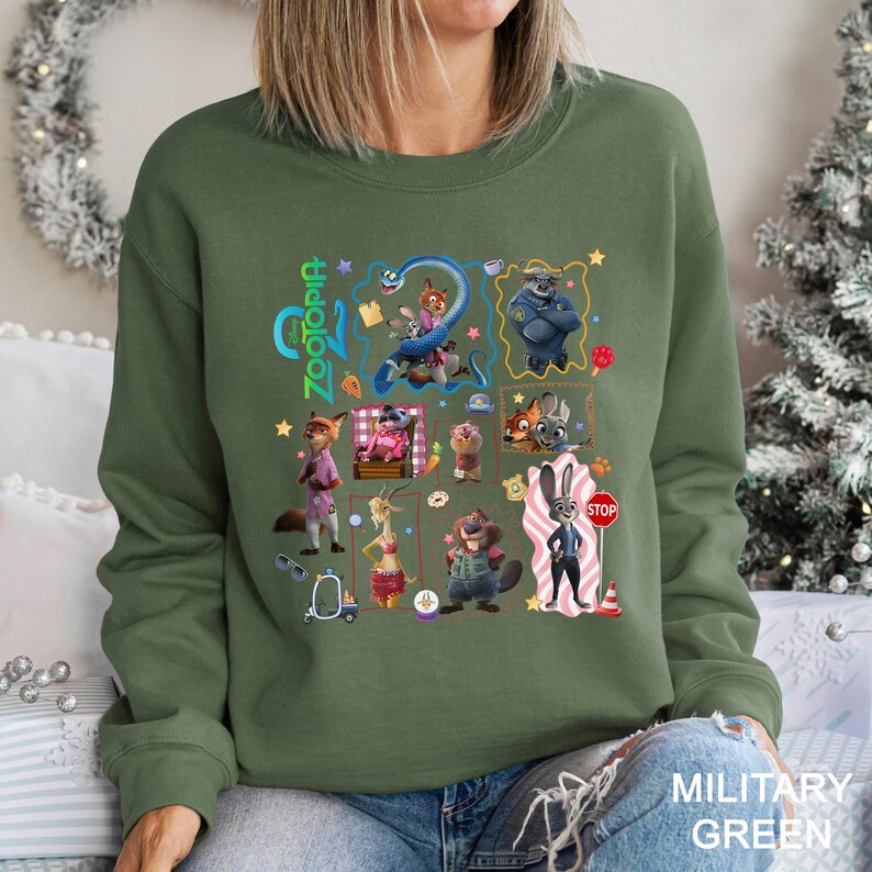 May include: Military green sweatshirt with a colourful graphic of characters from the animated film "Zootopia." The design includes the film's title and various characters in a grid-like arrangement. The sweatshirt is a crew neck style.