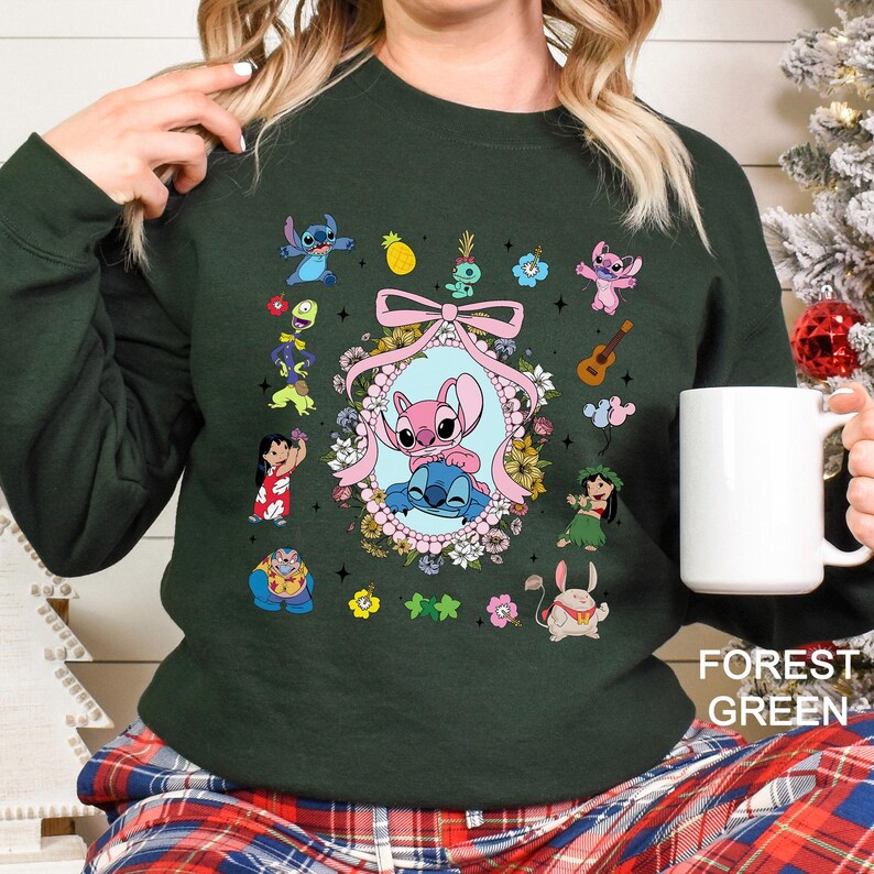May include: Forest green sweatshirt featuring a colorful graphic of Stitch and other characters from the Lilo & Stitch franchise. The design includes a central oval frame with Stitch characters, surrounded by flowers and a pink bow. The text "FOREST GREEN" is at the bottom.