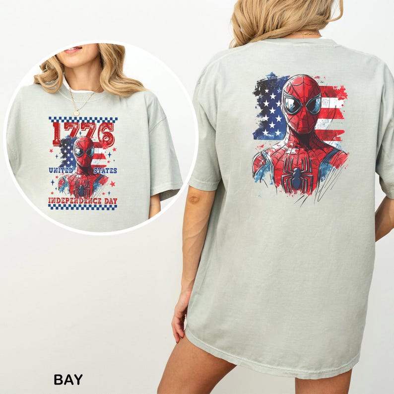 Może przedstawiać: Jasno szałwiowy t-shirt z grafiką maski superbohatera na tle stylizowanej amerykańskiej flagi. Przedni wz&oacute;r zawiera napis 1776 UNITED STATES INDEPENDENCE DAY, natomiast na plecach znajduje się większa wersja tej samej grafiki z superbohaterem.
