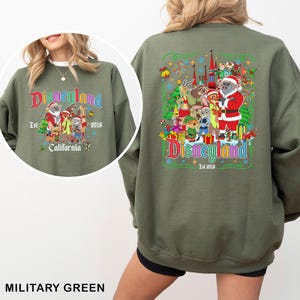 May include: Military green sweatshirt featuring a Disneyland graphic with Santa Claus and various Disney characters. The front and back of the sweatshirt display the Disneyland logo, the year 2016, and the word California.